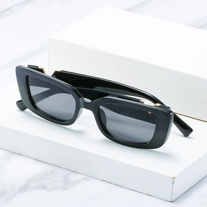 Square frame black sunglasses with gold metal accents on white marble stone display