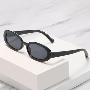 Lunettes de soleil ovales noires rétro avec verres gris foncé sur marbre blanc
