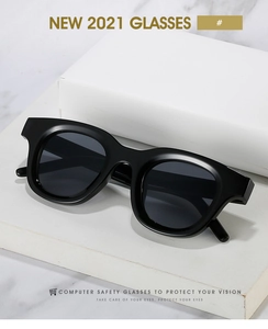 Detail of oval tea-green sunglasses with thick black frames on a marble surface