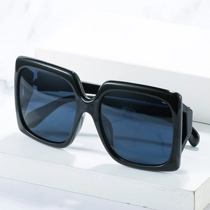 Lunettes de soleil carrées oversize avec monture noire et verres bleus sur marbre