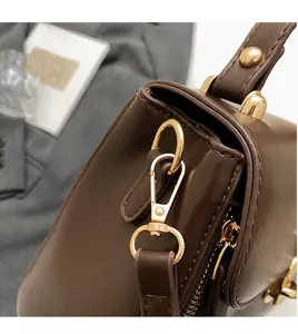 Detailed close-up of dark brown leather crossbody bag with high-shine gold metal hardware