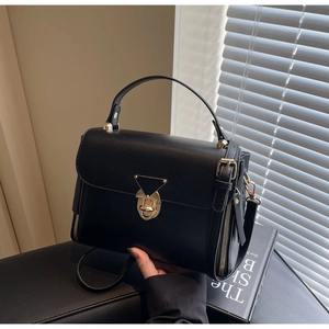 Detail view of black matte leather shoulder bag with a gold triangular lock closure
