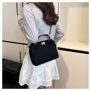 Detail of black suede handbag showing golden rectangle twist lock and smooth top handle
