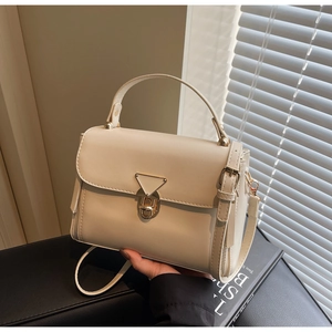 Close-up of cream crossbody bag with golden triangular lock and adjustable strap