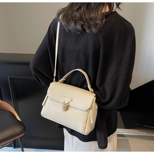 Detail of a creamy beige crossbody bag with a triangular metal lock shown on a model