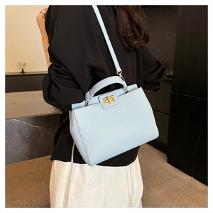Close-up of light blue pebbled leather bag with golden twist lock worn by a model