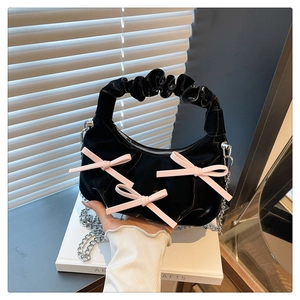 Detail of black glossy handbag featuring three pink bows and a ruched handle design