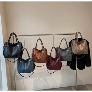 Row of large leather tote bags in six colors hanging on wall with silver hardware