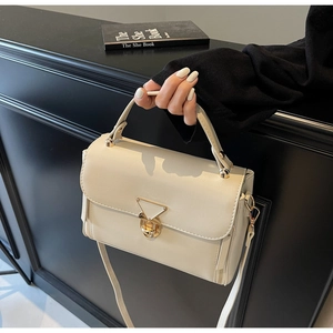 Detailed view of cream crossbody bag featuring a golden triangular twist lock on black surface