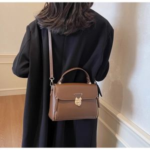 Detailed back view of a brown leather crossbody bag with golden triangle lock on model
