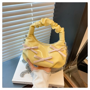 Detail of yellow glossy hobo bag with pink bows and elegant pleated handle