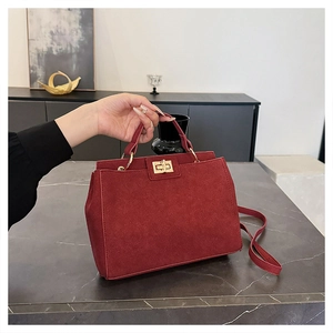 Detail of dark burgundy suede tote with gold twist lock on marble surface