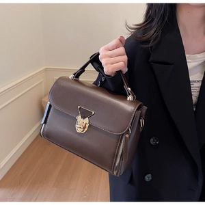 Detail of chocolate brown leather crossbody bag featuring gold triangle lock and zip detail