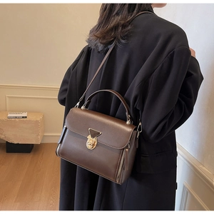 Detail of dark brown leather crossbody bag featuring a golden triangle lock and zippers
