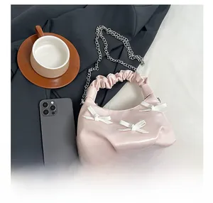 Pink pleated handbag with white bows and silver chain strap shown next to a smartphone