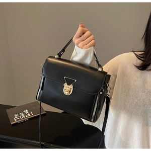 Detail of a black leather handbag with golden triangle lock and dual decorative side zippers