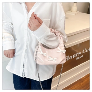 Detail of light pink shoulder bag with white bows and pleated handle in a cafe setting