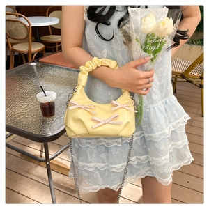 Detail of light yellow ruched handbag with pink bows and silver chain strap