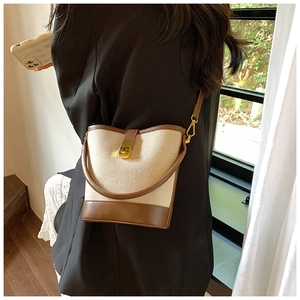 Close-up of a stylish cream canvas bucket bag with brown leather trim and gold lock