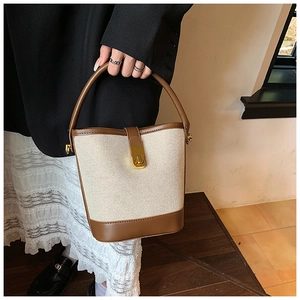 Detail of canvas and leather bucket bag featuring a gold metal twist lock and textured finish