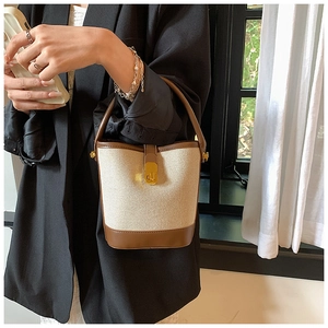 Detail of canvas bucket bag with leather trim, metal twist lock, and gold hardware