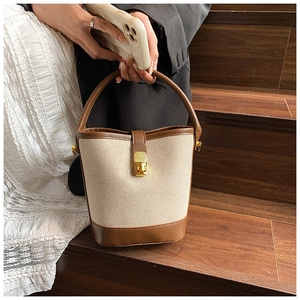 Close-up of woven bucket bag with brown leather trim and golden metal turn-lock closure