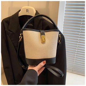 Detail of canvas bucket bag featuring beige fabric, black leather trim and gold twist lock