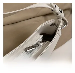 Detailed view of silver metal zipper and hardware on white leather underarm crescent bag
