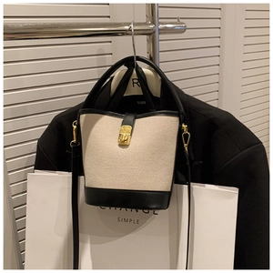 Detail of canvas bucket bag with black leather trim and gold metal buckle hardware