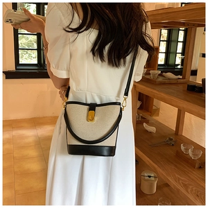 Modern beige canvas bucket bag with black leather trim worn by a woman in a white dress
