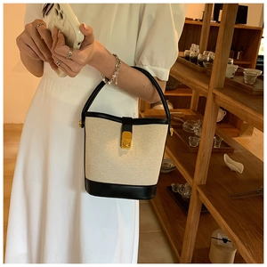 Detail of canvas bucket bag with black leather trim and golden metal turn-lock closure