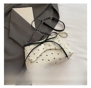 Vista detallada de bolso blanco texturizado con lazos negros y colgante de perlas
