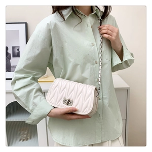White quilted crossbody bag with silver crystal buckle and chain strap on female model
