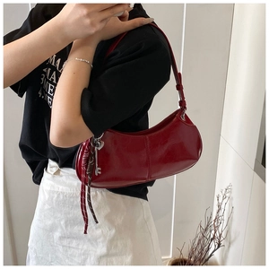 Detail of burgundy glossy leather crescent bag with silver heart charm and braided cord