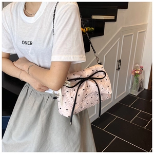 Bolso de hombro acolchado rosa con lazo negro y cadena mostrado puesto en el modelo