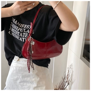 Close-up of deep red crescent moon shoulder bag with designer charms and glossy finish