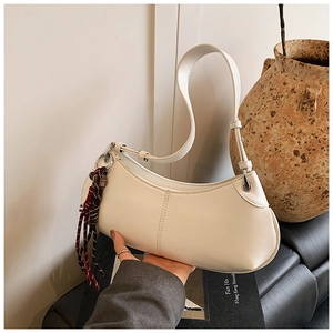 Detail of white leather crescent bag featuring a decorative woven tassel and stitching