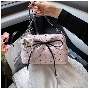Detalle del bolso bandolera plisado rosa con un lazo negro grande y un colgante de corazón