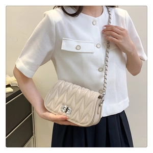 Chic quilted beige shoulder bag with silver chain strap worn by a female model