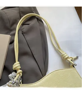 Detail of light yellow leather shoulder bag with decorative pearl and lace bow charms
