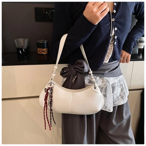 Close-up of a white crescent moon shoulder bag with decorative woven pendant detail