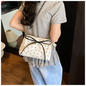 Detalle del bolso beige acolchado con lazos negros y correa de cadena metálica