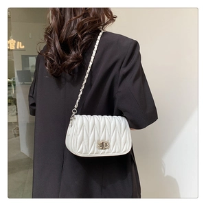 Detail of white matelassé quilted bag with sparkling rhinestone lock and chain strap
