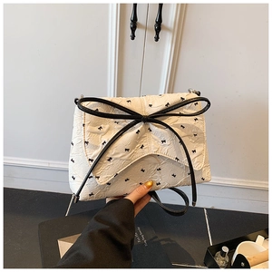 Detalle macro del bolso blanco plisado con un gran lazo negro y estampados de cintas