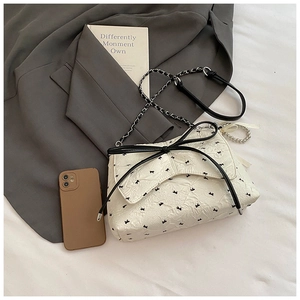 Detalle del bolso plisado blanco con lazos negros y correa de cadena metálica elegante
