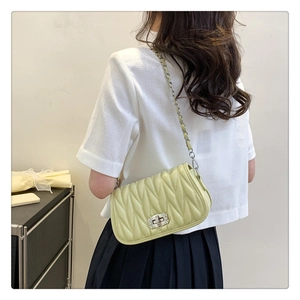 Detail of pistachio green quilted chain bag with rhinestone lock worn as crossbody