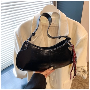 Detail of black crescent shoulder bag featuring heart charm and red white rope knot