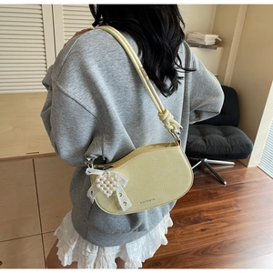Detail of yellow curved underarm bag with decorative pearl and lace bow pendant charm