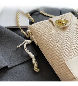 Close-up of woven cream bucket bag featuring golden peanut charm and leather chain