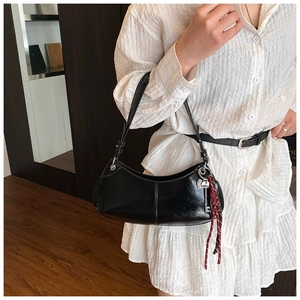 Close-up of black patent leather moon bag with silver key charm and woven pendant